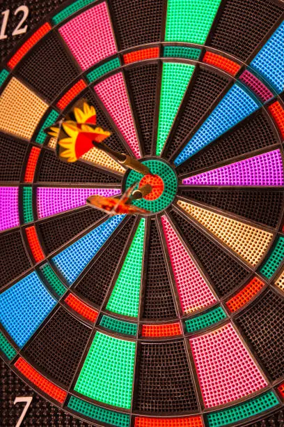 Photo of multicolored darts board with two darts in the center of the target