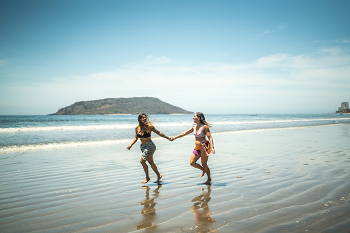 Lesbian couple running by the sea holding hands