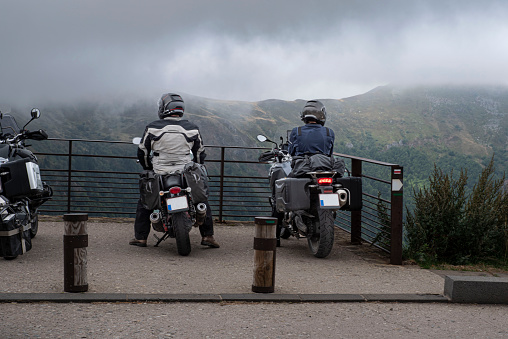 Two bikers stopped to watch the mountain landscape under the clouds