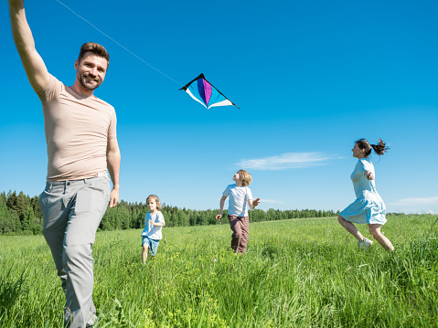 Parents and children running with kite on summer holiday vacation, perfect meadow and sky on seaside