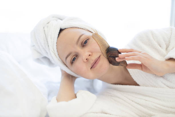 istock Lady lying on bed with snail on face skin indoors 1484543449