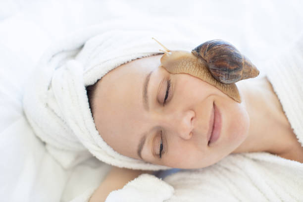 istock Lady having fun with snail on cheek skin indoors 1484543459