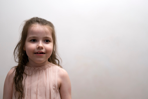 close-up studio portrait of a 9 year old girl with long brown hair in a gray dress on a beige background