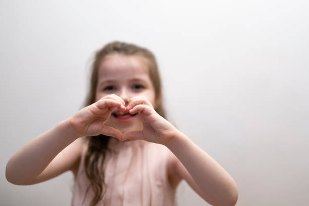 una ragazza, una bruna di sette anni, mostra la figura di un cuore con le mani. - 6 7 years little girls child portrait foto e immagini stock
