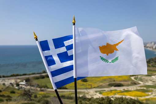 Flags of Greek and Cyprus fluttering in front of blue sea, sky and landscape