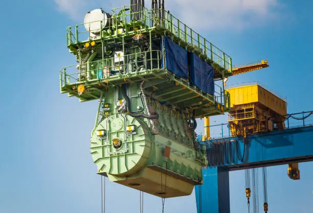 Transportation of a large marine engine by a port crane using steel cables.