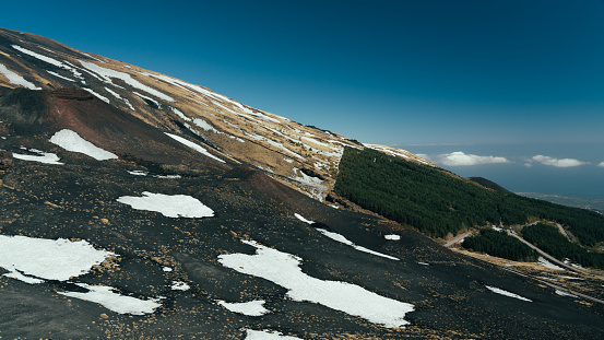 Panorama of uneven ground full of lava earth and craters. Small shrubs and large furrows, mediterranean climate. Colorful mountain trails on southern slope.