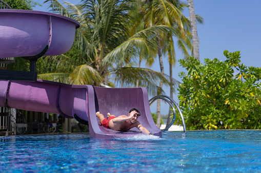 A young man with the sun glasses in his hands slides down a pipe in a water park at a hotel in the Maldives.