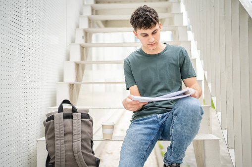 One Young man teenager caucasian student with books read study at campus in day sit on staircase education concept copy space
