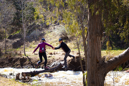 Santa Fe, NM: A brave (or naive?) couple crossing rapids on a wet log over the Santa Fe River, which is running much faster in 2023 than normal.