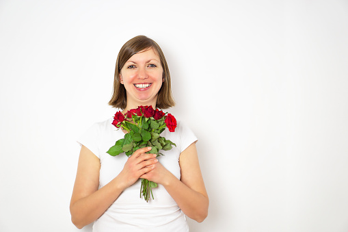 Portrait of happy smiling girl in white shirt with bouquet of red roses in hands. High quality photo.