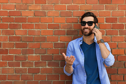 Happy man talking on phone near red brick wall. Space for text