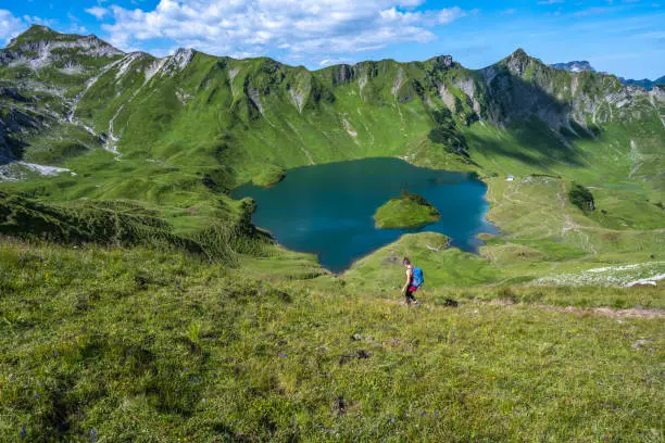 Description: Hiker walks on alpine path in beautiful morning atmosphere at a beautiful mountain lake. Schrecksee, Hinterstein, Allgäu High Alps, Bavaria, Germany.