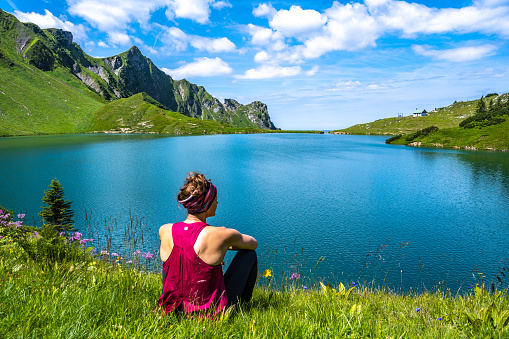 Description: Woman enjoys scenery at beautiful turquoise mountain lake in the afternoon. Schrecksee, Hinterstein, Allgäu High Alps, Bavaria, Germany.