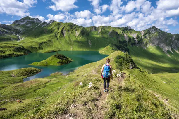 Description: Hiker walks on alpine path in beautiful morning atmosphere at a beautiful mountain lake. Schrecksee, Hinterstein, Allgäu High Alps, Bavaria, Germany.
