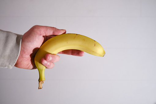 Male hands hold a yellow banana. Fresh fruits on a light background. Close-up