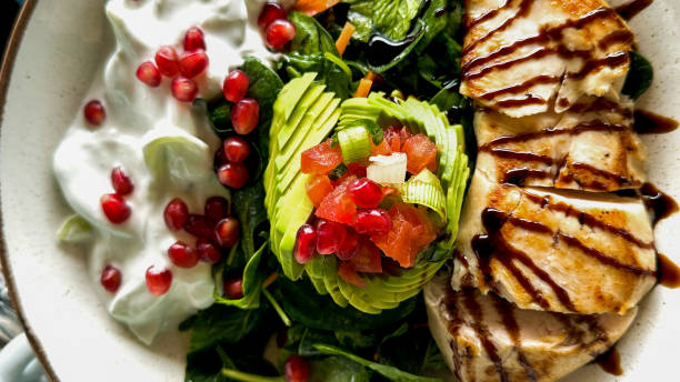 Grilled chicken served with Greek yoghurt, pomegranate seeds, avocado slices, tomatoes, onions, and green salad close-up stock photo
