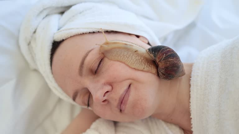 Female doing snail facial procedure after massage on bed