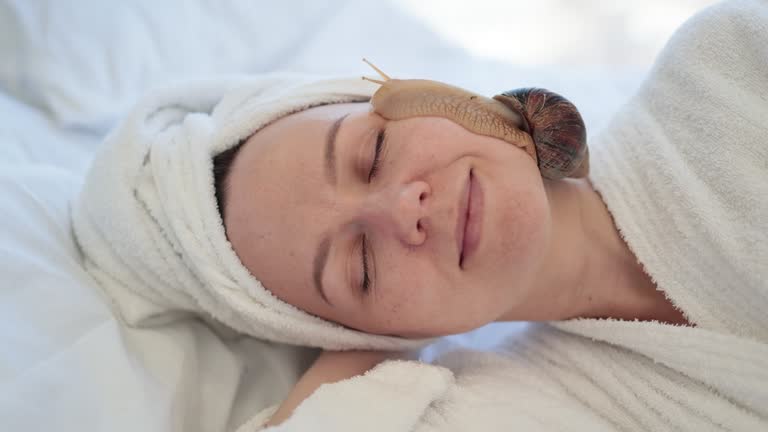 Female doing snail facial procedure after massage on bed