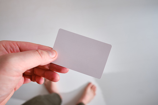 A man holds a business card close-up on a light background. Place for text. Mockup