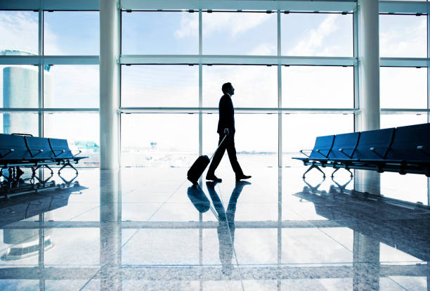 View on the aiport window with woman walking with suitcase at the departure hall during the sunset. Wide angle view with copy space