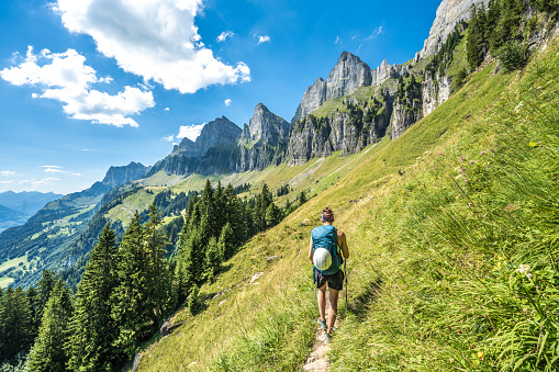 Description: Sporty woman walks on scenic hiking trail between meadow and trees and the Churfürsten mountain range in the background. Schnürliweg, Walensee, St. Gallen, Switzerland, Europe.