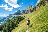 Sporty woman walks on scenic hiking trail between meadow and trees and the Churfürsten mountain range in the background. Schnürliweg, Walensee, St. Gallen, Switzerland, Europe.