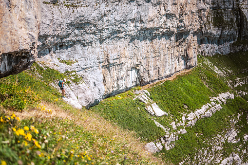 Description: Athletic woman hikes along hike trail below steep rock wall. Schnürliweg, Walensee, St. Gallen, Switzerland, Europe.