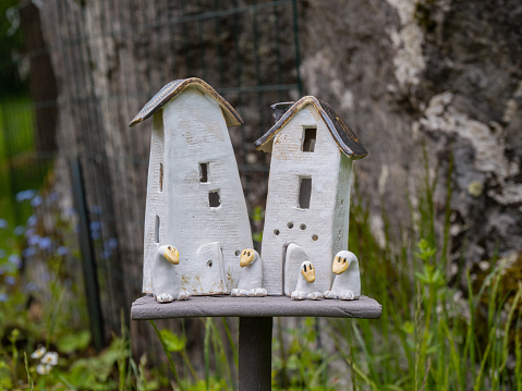 Angelsberg, Sweden - May 28, 2022: A vibrant garden in focus, with ceramic houses and a small birdhouse set among the plants. A goose watches from afar.