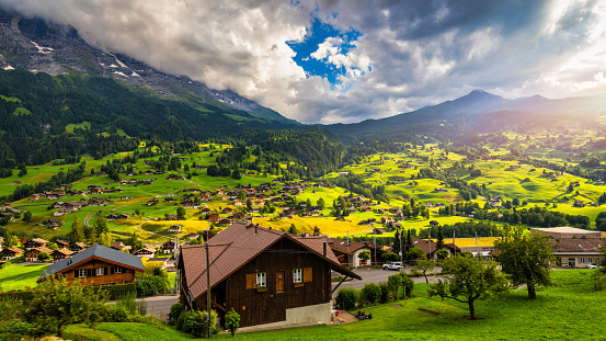 Grindelwald village view and summer Swiss Alps mountains panorama landscape, wooden chalets on green fields and high peaks in background, Switzerland, Bernese Oberland, Europe.