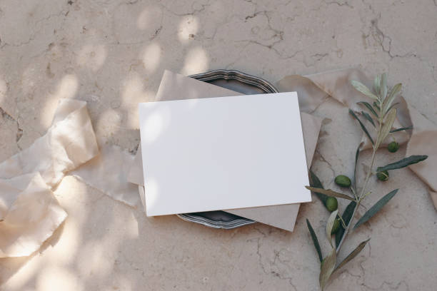 istock Mediterranean wedding stationery. Birthday mock-up. Blank greeting card, envelope on silver plate. Dappled light. Olive tree branches, fruit. Beige marble background, floor. Summer holiday design. Top 1484653656