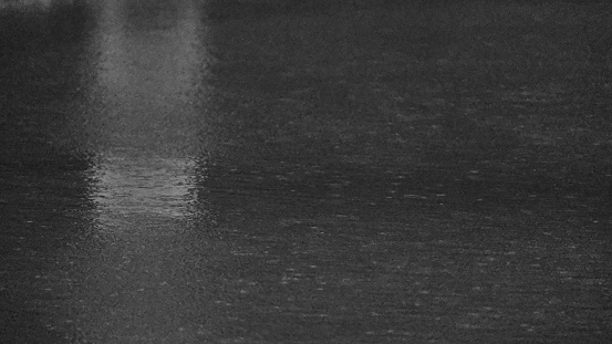 Black and white image of rain creating a ripple effect in puddle of water