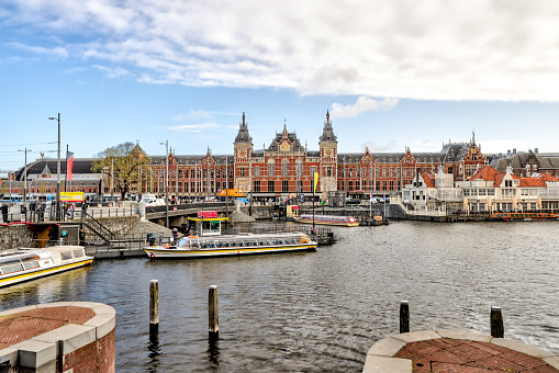 Amsterdam, Netherlands - March 28, 2023: Tour boats in the canals in front of the historic Amsterdam Centraal rail terminal