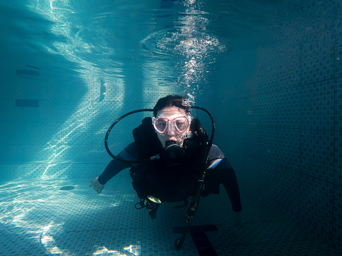 Portrait of woman looking at camera in wetsuit while practicing in pool. Practical course in swimming pool