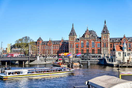 Amsterdam, Netherlands - March 28, 2023: Tour boats in the canals in front of the historic Amsterdam Centraal rail terminal