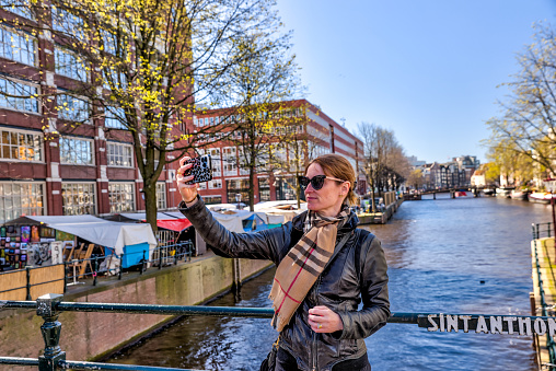 Amsterdam, Netherlands - March 28, 2023: A young blonde woman taking a selfie along the canals in Amsterdam