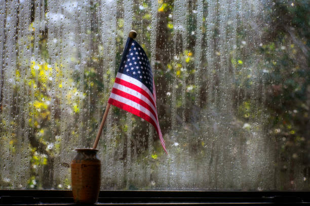 Small American flag inside a ceramic jar by a window on a rainy day.