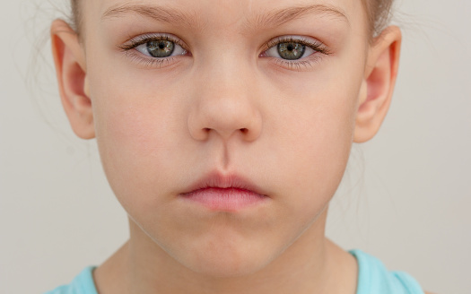 Serious child face with closed lips cropped head caucasian little girl of 6 7 years on grey background