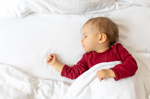 Infant baby sleeping in bed with white linen, children's daytime sleep.