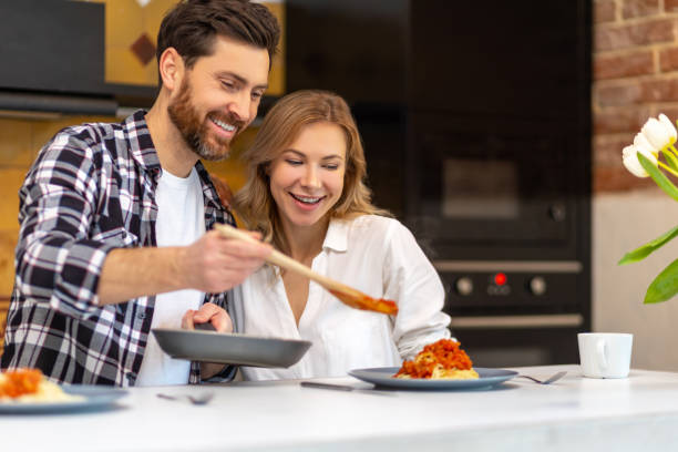istock Young couple having breakfast in kitchenn, man serving dinner, woman sitting at table. 1484692498