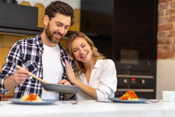 istock Young couple having breakfast in kitchenn, man serving dinner, woman sitting at table. 1484692509