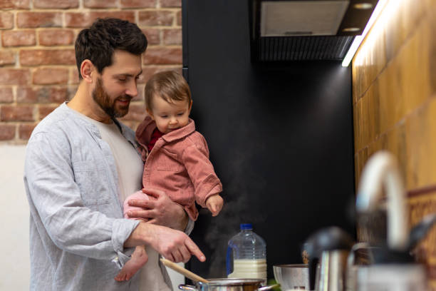istock Bearded man cooking dinner with baby daughter in hands standing in kitchenn. 1484692521