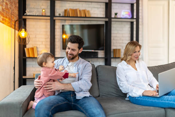 istock Father carrying infant daughter mother using laptop remote work husband helping with baby child 1484692566