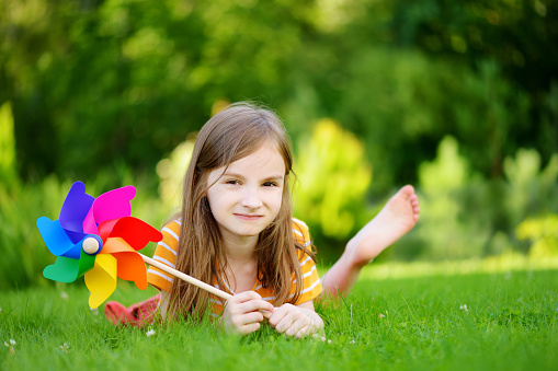 Adorable little girl holding colorful toy pinwheel on warm and sunny summer day