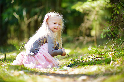 Adorable little girl picking the first flowers of spring in the woods on beautiful sunny spring day. Cute child having fun outdoors.