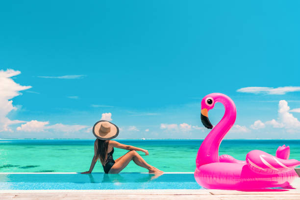 istock Vacation summer fun woman sunbathing with inflatable pink flamingo pool float by infinity swimming pool. Luxury travel holiday at overwater villa resort. 1484706786