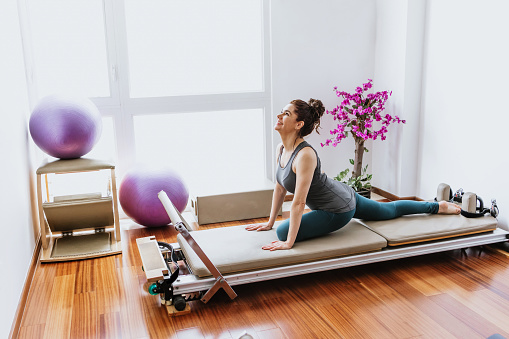 latin woman doing pilates exercises on reformer bed at home in Mexico, hispanic people