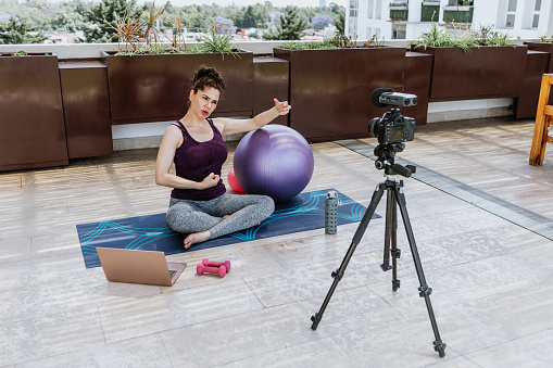 Latin woman recording workout exercise with video camera in terrace at home in Mexico, hispanic people