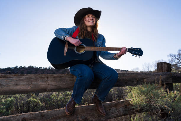 woman playing guitar sitting on fence - musica sertaneja imagens e fotografias de stock