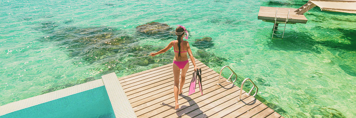 Luxury Bora Bora resort woman going snorkeling from overwater bungalow panoramic. Tahiti paradise destination vacation.